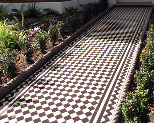 Black and White Victorian checker board path tiles. Victorian black and white tiles with zigzag border, bordered by rope-top edging and newly planted garden shrubs.
